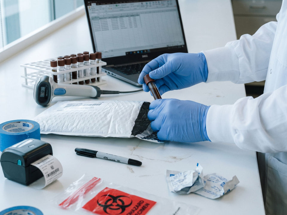 Logging a returned sample: gloved hands take the collection tube out of its return mailer